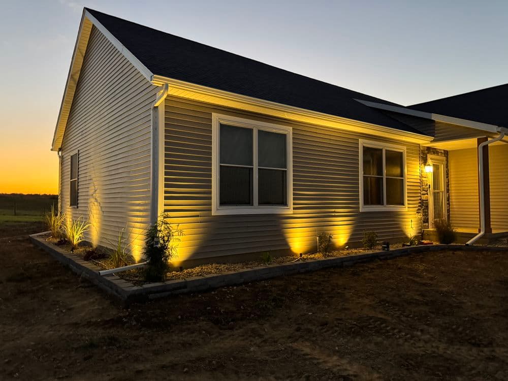 Modern home exterior with landscape lighting at sunset, showcasing warm illumination.