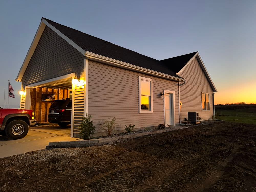 Newly built modern house at sunset with garage and landscaping, featuring a red truck.