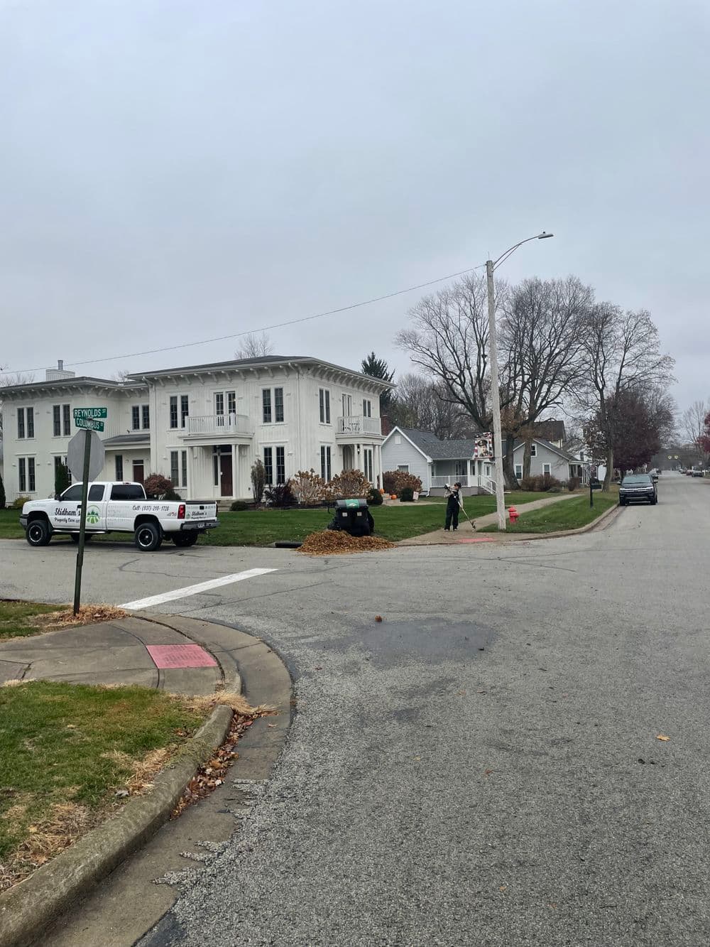 Lawn maintenance crew raking leaves in residential neighborhood on a cloudy day.