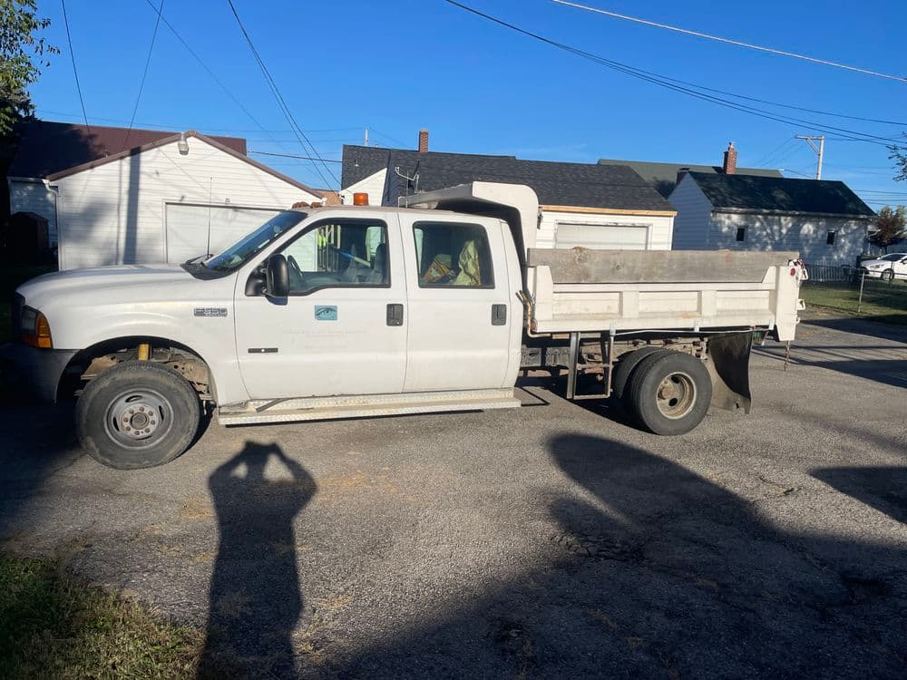 White dump truck parked on a residential street with garages in the background.