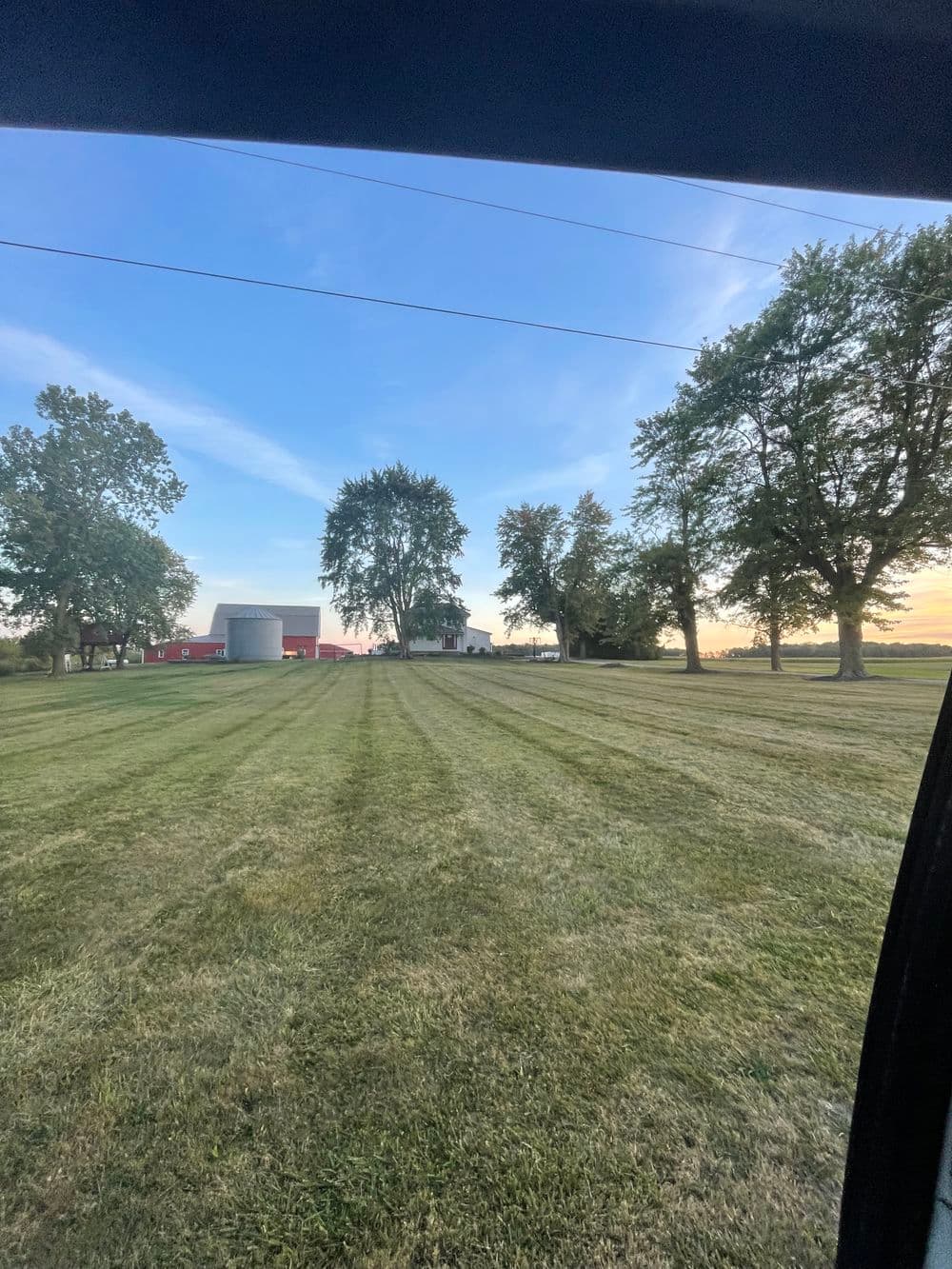 Scenic farmland with freshly mowed grass, trees, and a barn under a clear blue sky.