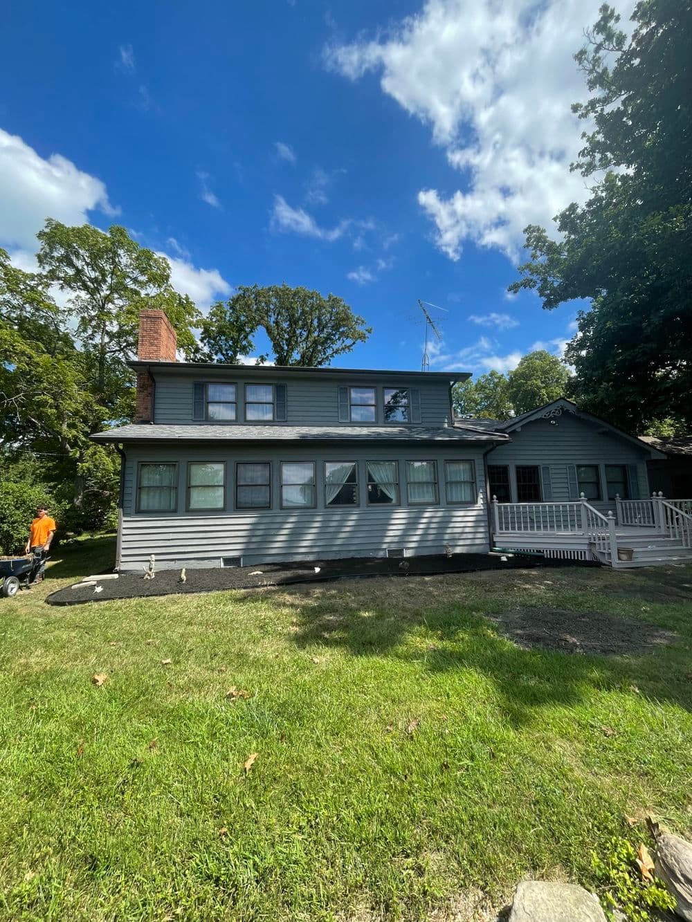Renovated two-story gray house with a porch and green lawn under a blue sky.