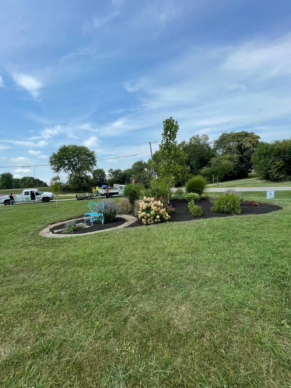 Colorful garden landscape with seating area, trees, and shrubs under a blue sky.