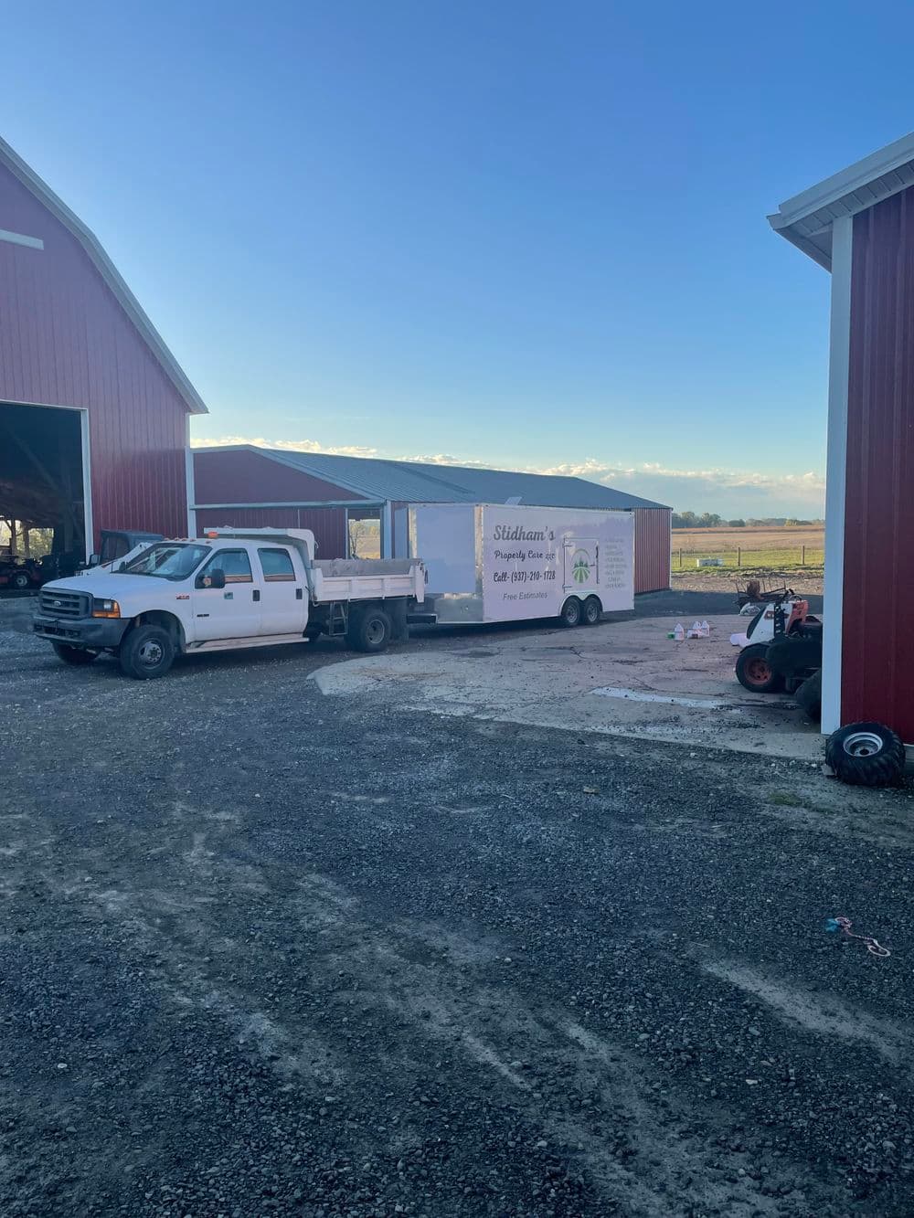 Truck and trailer with farm equipment near red barns on a rural farm.