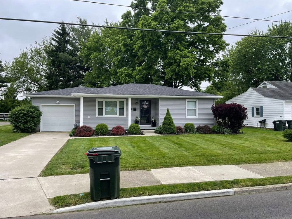 Single-story gray house with manicured lawn, garage, and nearby green trees.
